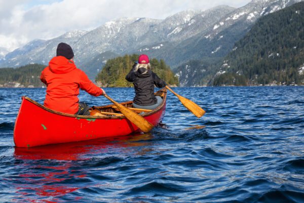 Couple friends on a wooden canoe are paddling in an inlet surrounded by Canadian mountains. Taken in Indian Arm, near Deep Cove, North Vancouver, British Columbia, Canada.