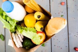 Grocery shopping concept. Different food in paper bag on wooden background. Top view