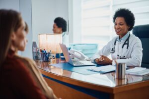 Happy African American female doctor talking to mother and son during medical appointment at pediatrician's office.