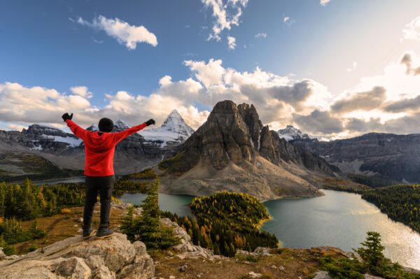 Man traveler stand with raised hands on Niblet with Mount Assiniboine in provincial park at Alberta, Canada